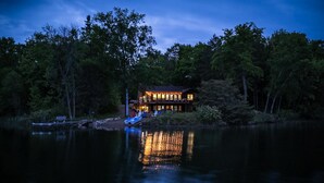 A lakeside lodge with a reflective pool in front, surrounded by trees. - Lake House w/Hot Tub, Game Room, Fireplace & Beach (Crosby)