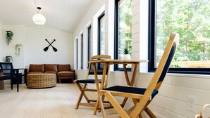 A room with a wooden floor, a brown leather sofa, a wicker ottoman, two wooden chairs with blue cushions, a small table, and a potted plant. - Lake House w/Hot Tub, Game Room, Fireplace & Beach (Crosby)