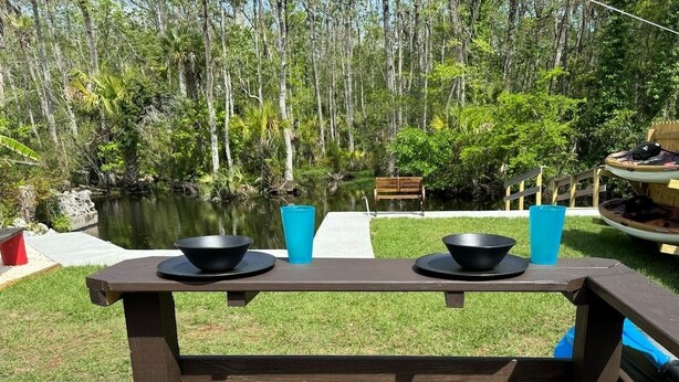 A wooden picnic table with two stools, two black bowls, and two blue cups. - Waterfront Multi-family Retreat (Crystal River)