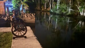 A calm water body with a wooden cart on a concrete path, surrounded by trees and a building with illuminated windows. - Waterfront Multi-family Retreat (Crystal River)