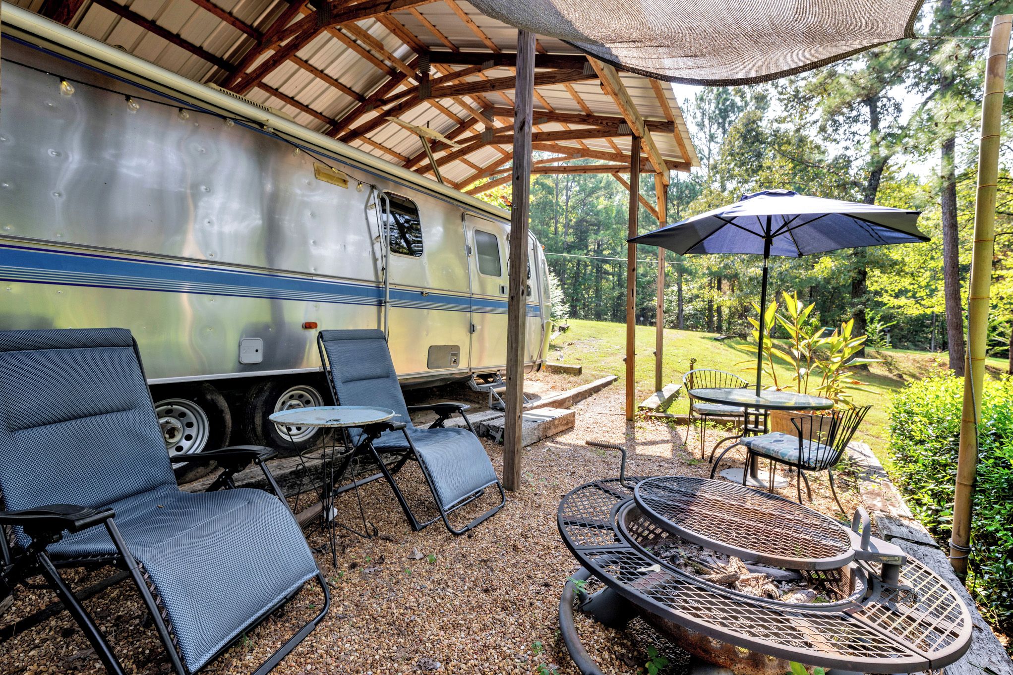 Un espacio al aire libre cubierto con una caravana, asientos y un hogar para fuego.