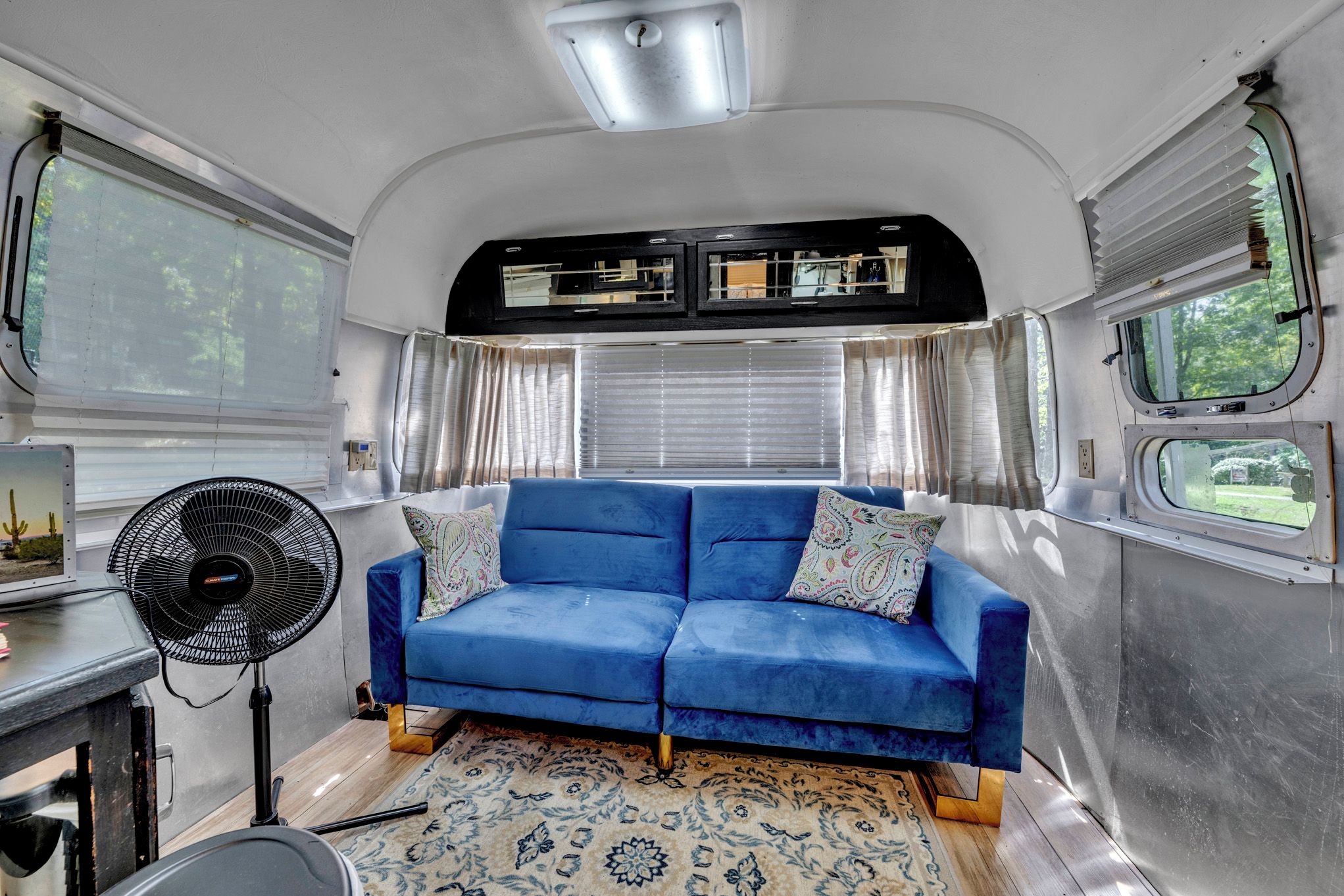 A compact living space with a blue sofa, a fan, and a patterned rug.