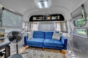 Un espace de vie compact avec un canapé bleu, un ventilateur et un tapis à motifs.