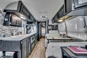 A compact RV interior with a kitchenette, a dining area, and a small bedroom.
