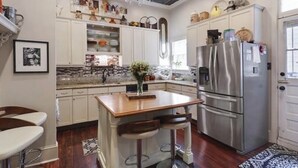 A modern kitchen with white cabinets, a central island with bar stools, stainless steel appliances, and decorative items on shelves. - Charming 2-bedroom apartment with AC, WiFi in wonderful New Orleans (New Orleans)