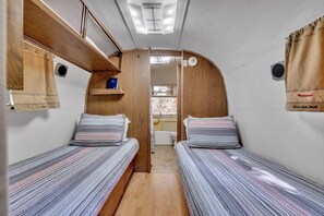 Interior compacto de una caravana con dos camas, un kitchenette pequeño y una ventana.