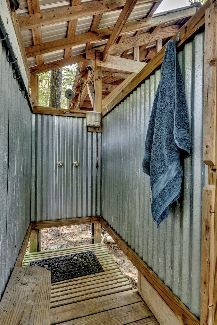 A small, enclosed wooden structure with a corrugated metal wall, a wooden bench, and a towel hanging on the wall.