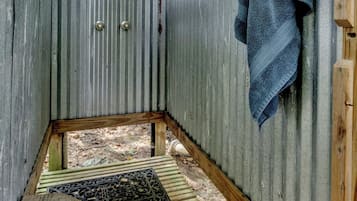 A small, enclosed wooden structure with a corrugated metal wall, a wooden bench, and a towel hanging on the wall.