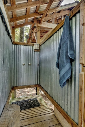 A small, enclosed wooden structure with a corrugated metal wall, a wooden bench, and a towel hanging on the wall.