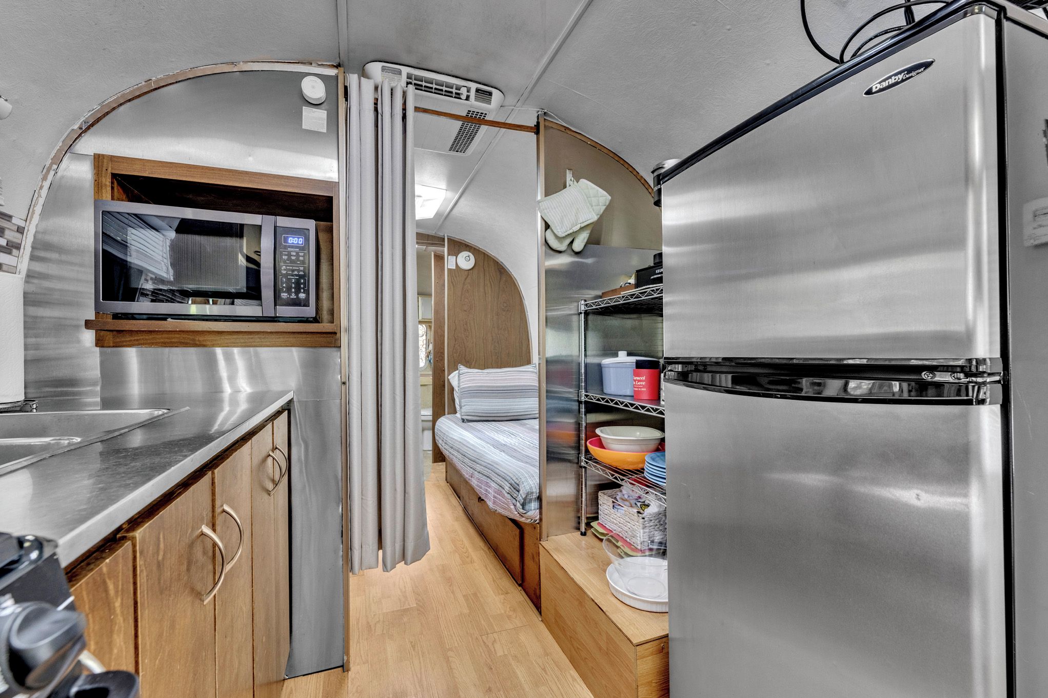A compact kitchenette with a microwave, a refrigerator, and a small bed.