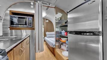 A compact kitchenette with a microwave, a refrigerator, and a small bed.