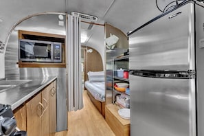 A compact kitchenette with a microwave, a refrigerator, and a small bed.