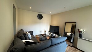 A modern living room with a grey sofa, a flat-screen TV, a coffee table, and a large mirror.