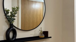 A round mirror with a black frame, a potted plant, and a small shelf with a bottle and a cup.