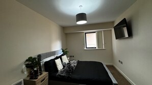 A bedroom with a bed, a bedside table with a plant, a window, and a ceiling light.