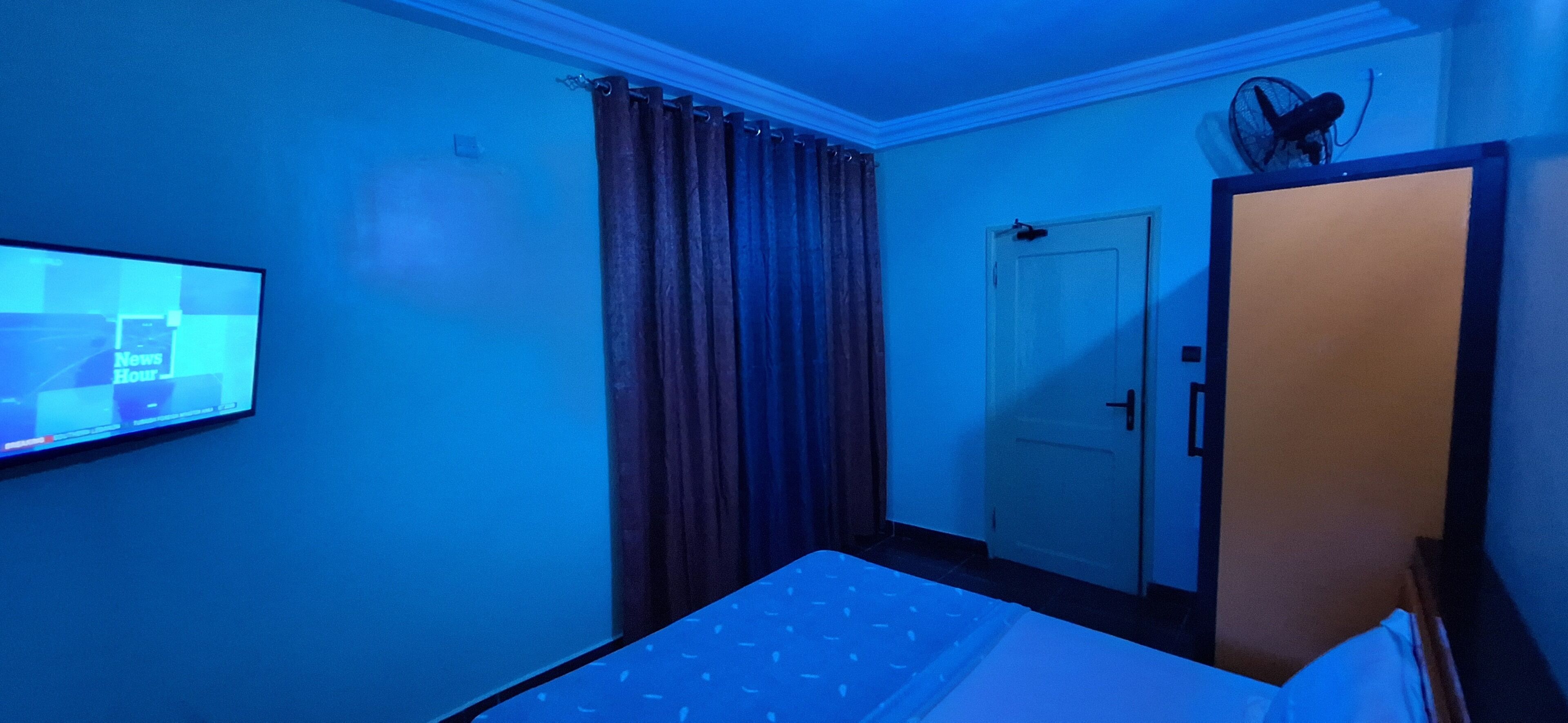 Una habitación con una cama, un televisor montado en la pared, una puerta y un ventilador en el techo.