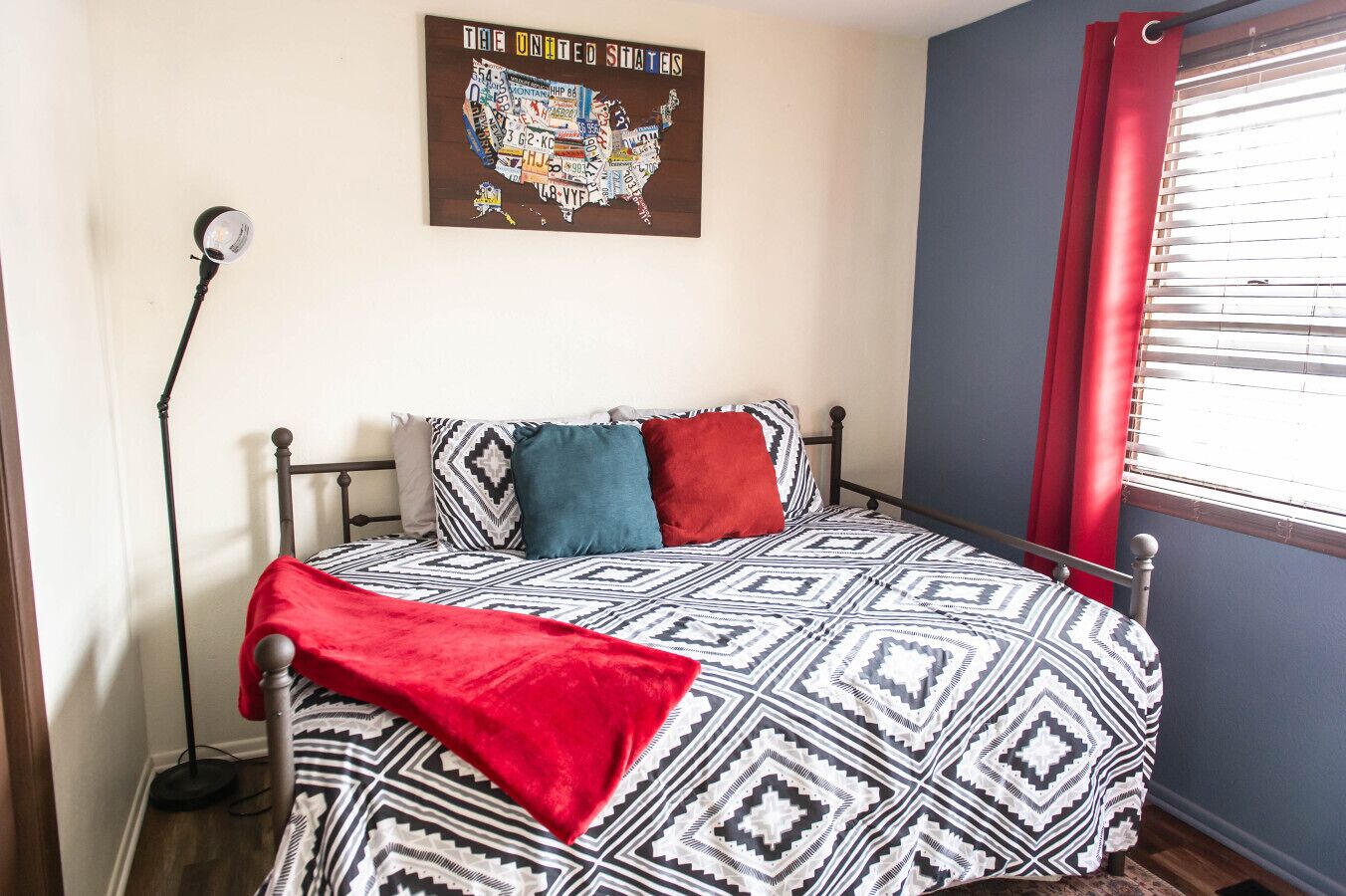 A bedroom with a patterned bedspread, a red throw blanket, and a map of the United States on the wall.