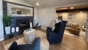 A living room with a fireplace, a blue armchair, a brown sofa, and a wooden ceiling. - Lake Life! (Wautoma)