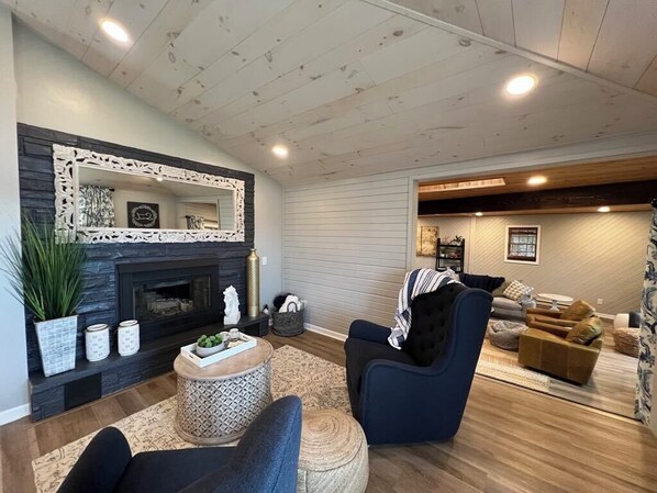 A living room with a fireplace, a blue armchair, a brown sofa, and a wooden ceiling. - Lake Life! (Wautoma)