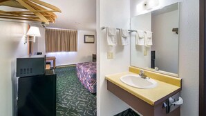 Una habitación de hotel con cama, escritorio, cómoda, espejo y baño con lavamanos y toallas.