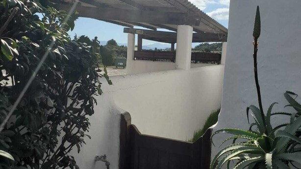 A white building with a wooden gate, a pergola, and surrounding greenery. - Apartment 2 min walk from cabo negro beach. (Tetouan)