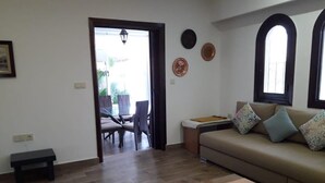A living room with a sofa, a coffee table, a bench, and a dining area with chairs and a table. - Apartment 2 min walk from cabo negro beach. (Tetouan)
