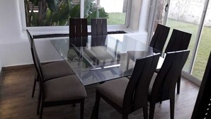 A modern dining area with a glass table and dark chairs, large windows, and a view of greenery outside. - Apartment 2 min walk from cabo negro beach. (Tetouan)