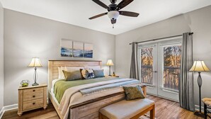 Un dormitorio con cama de madera, ventilador de techo, lámparas de noche, un banco y vistas por una ventana.