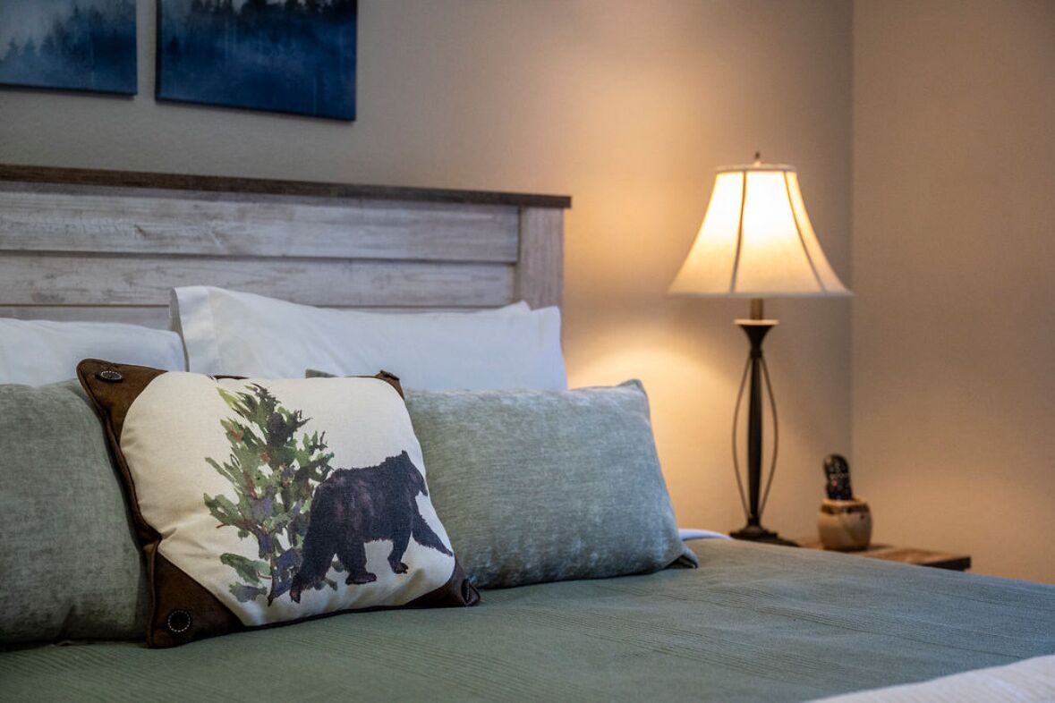 A bed with a wooden headboard, two pillows, a lamp, and a small table with a vase.