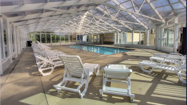 Un área de piscina cubierta con sillones reclinables blancos y techo de cristal.