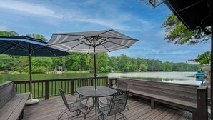 A wooden deck with a round table and chairs, an umbrella, and a view of a lake. - Lakeside Country Cottage (Talking Rock)