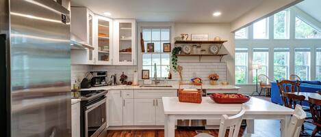 A modern kitchen with white cabinetry, stainless steel appliances, and a dining area with white chairs and a table.