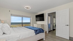 Een slaapkamer met een bed, een aan de muur bevestigde televisie, een raam met uitzicht en een deur naar een andere kamer.