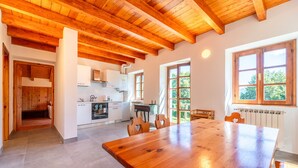 Una cocina amplia con vigas de madera, un comedor con una gran mesa de madera y ventanas que dan a zonas verdes.