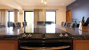 A modern kitchen with a central island, a built-in oven, and a dining area with a glass table and chairs. - A-409 Enjoy Your Vacation In This Exquisite Condominium! (Cabo San Lucas)