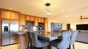 A modern kitchen with a central island, bar stools, stainless steel appliances, and a large flat-screen TV. - A-409 Enjoy Your Vacation In This Exquisite Condominium! (Cabo San Lucas)