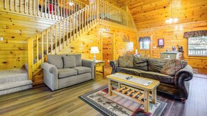 A wooden cabin interior with a staircase, two sofas, a coffee table, and a small table with a lamp. - Community Pool! Sevierville Stay w/ Hot Tub (Sevierville)