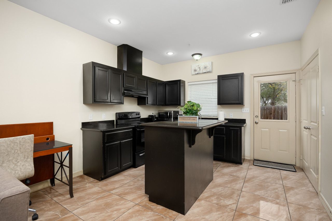 Uma cozinha compacta com armários escuros, uma ilha central e um espaço de jantar com uma mesa e cadeira.