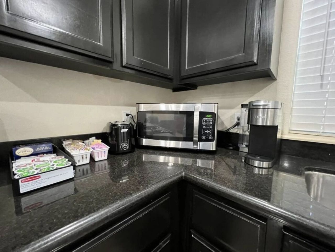 A kitchen with dark cabinets, a stainless steel microwave, a coffee maker, and a box of tea bags.