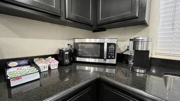 A kitchen with dark cabinets, a stainless steel microwave, a coffee maker, and a box of tea bags.