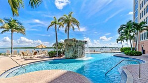 A pool area with a waterfall feature, lounge chairs, and palm trees. - Beautiful 1-bedroom condo with the best views ocean,back bay & beautiful sunset (Fort Myers Beach)