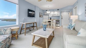 A spacious living room with a large window, a ceiling fan, a TV, a dining area, and a kitchen with an oven. - Beautiful 1-bedroom condo with the best views ocean,back bay & beautiful sunset (Fort Myers Beach)