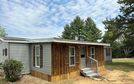 A single-story mobile home with a wooden front porch and a small set of stairs leading to the entrance.