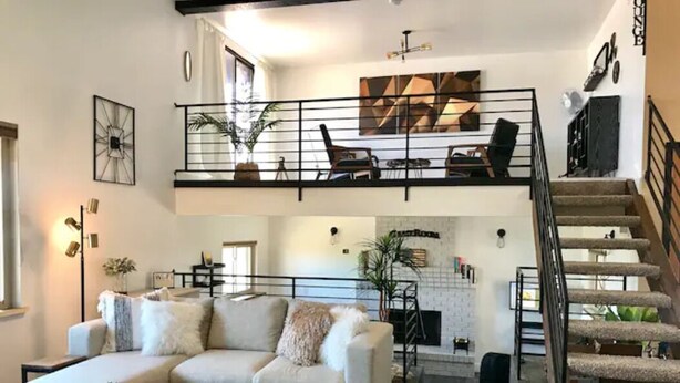 Ein geräumiges Wohnzimmer mit hohen Decken, einer Treppe und einem Kamin.