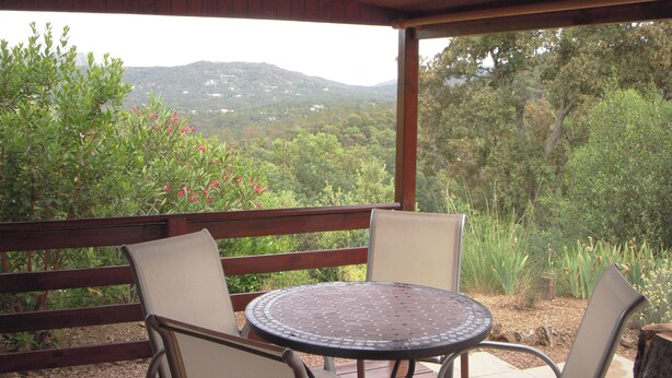 A covered patio with a round table and two chairs, overlooking a mountainous landscape.