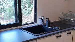 A kitchen with a black sink, white cabinets, and a window with a view of greenery.