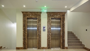 Un hall d’entrée avec deux ascenseurs, un escalier et un panneau de signalisation verte indiquant la sortie.
