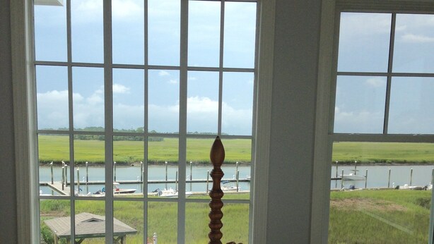 A bedroom with a large window overlooking a body of water and grassy fields.