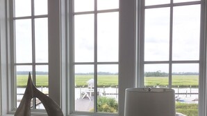 A room with a view of a green field and a body of water through large windows.