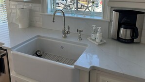 A kitchen with a large window, white cabinets, a sink, and a coffee maker.